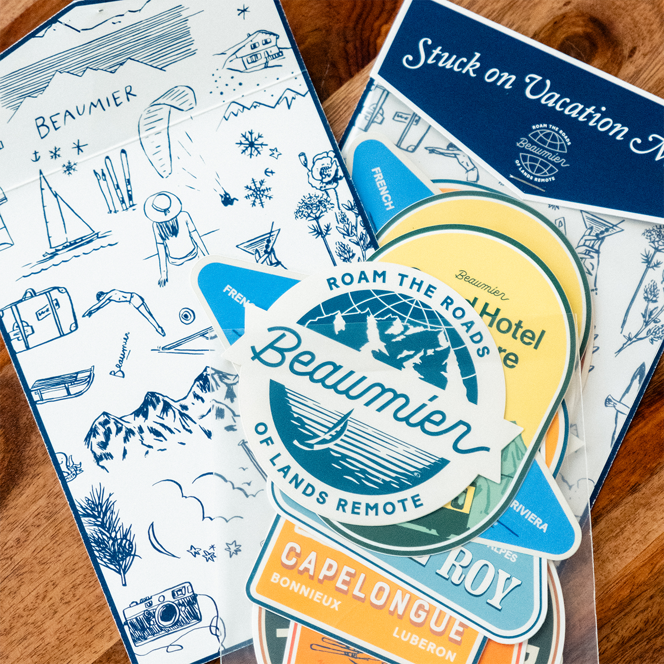 A collection of colorful travel-themed stickers as a sticker pack from "Beaumier" on a wooden surface.