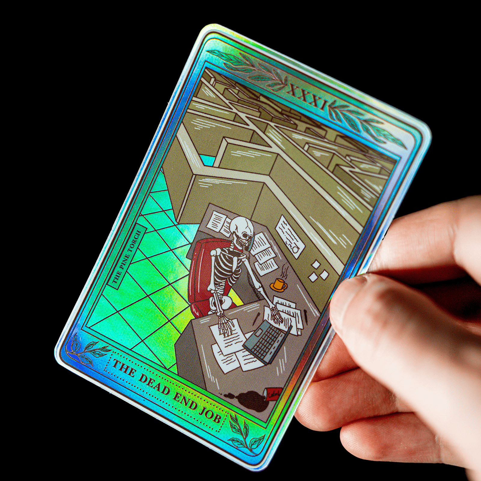 Hand holding a holographic tarot card sticker titled "The Dead End Job" with a skeleton at an office desk